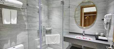 Un baño moderno con ducha de vidrio, inodoro, lavamanos con espejo y secador de pelo en la pared.