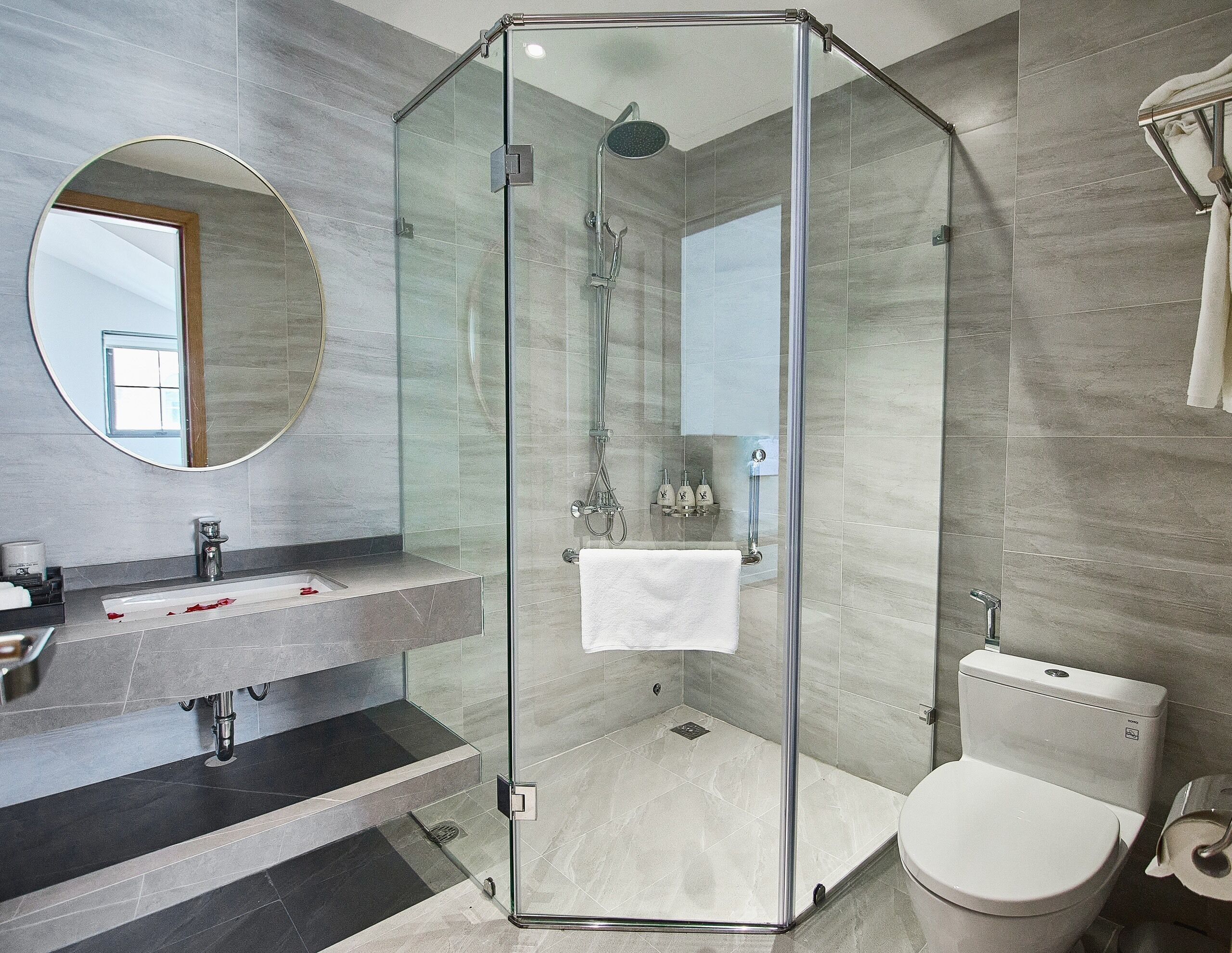 A modern bathroom with a glass-enclosed shower, a sink with a marble countertop, and a toilet.