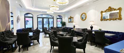 A luxurious hotel lobby with marble flooring, black upholstered chairs, a blue sofa, and ornate chandeliers.