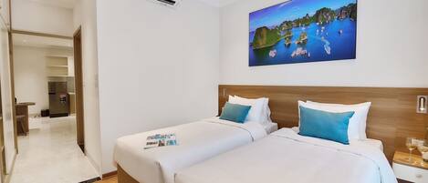 A hotel room with two beds, a painting of a coastal scene, a wooden headboard, and a nightstand with glasses.