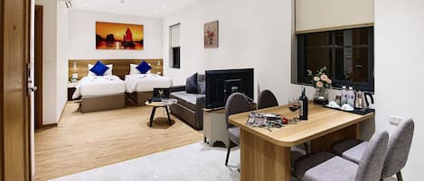 A hotel room with two beds, a desk, a TV, and a dining area.