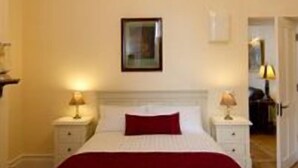 Una habitación de hotel con una cama grande, dos mesitas de noche con lámparas, un cuadro en la pared y una puerta que da a otra habitación.