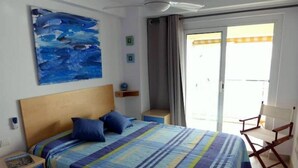 Een slaapkamer met een bed, nachtkastje, stoel, schilderij en uitzicht.