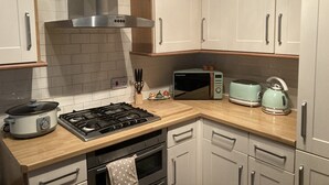 Een keuken met witte kastjes, een fornuis, een magnetron en een waterkoker.