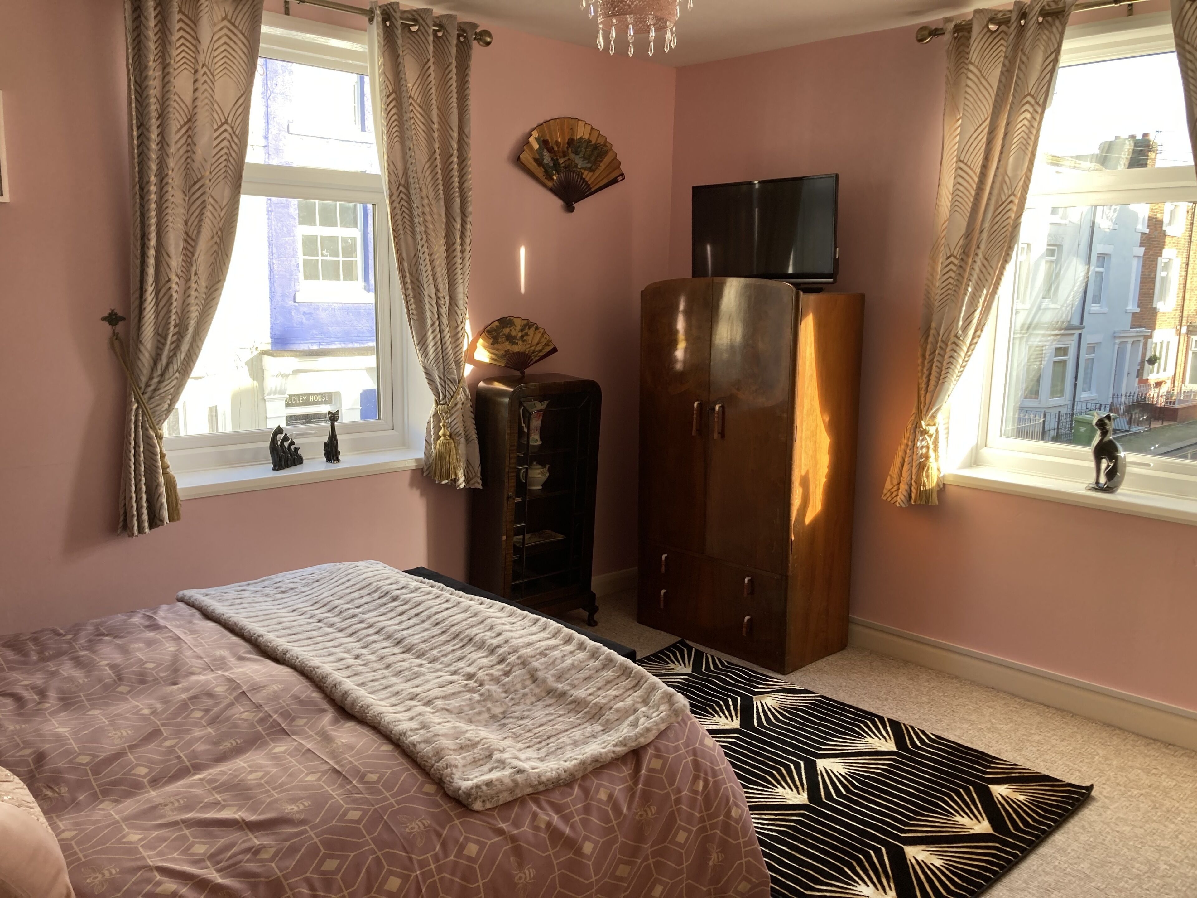 A bedroom with a bed, wardrobe, TV, and windows with curtains.