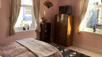 A bedroom with a bed, wardrobe, TV, and windows with curtains.