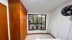 A bedroom with a large window, a wooden wardrobe, and a bed with a white comforter. - Apartamento Casa del Bosque (Cali)
