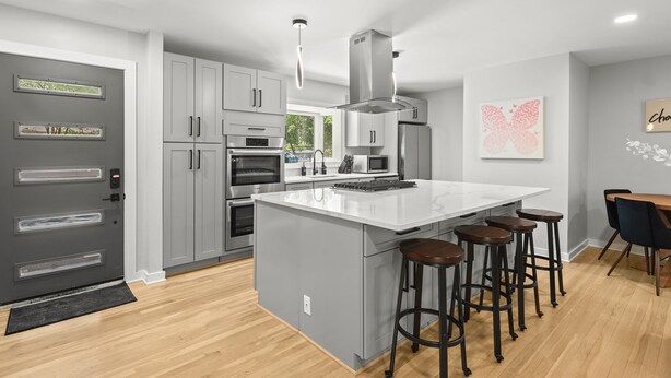 A modern kitchen with grey cabinets, a large island with stools, a built-in oven, and a microwave. - Modern, Cozy Buckhead 4+3 SFH + Backyard (Atlanta)