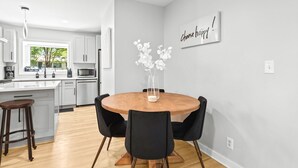 A modern kitchen with white cabinets, a wooden dining table with black chairs, and a vase with white flowers. - Modern, Cozy Buckhead 4+3 SFH + Backyard (Atlanta)