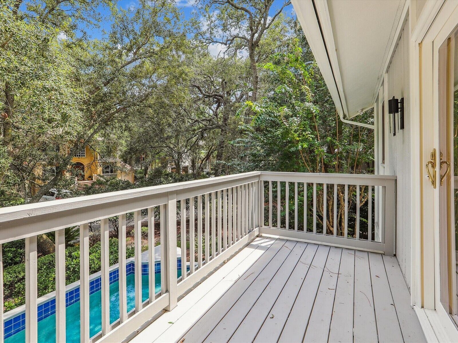 Une terrasse en bois avec une balustrade blanche, donnant sur une piscine et une végétation luxuriante.