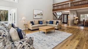A spacious living room with a high ceiling, a wooden staircase, and a dining area.
