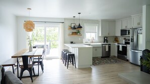 A modern kitchen with white cabinets, stainless steel appliances, and a dining area with a wooden table and chairs.