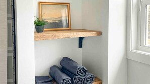A bathroom with a white arched shelf holding a framed picture and rolled towels.