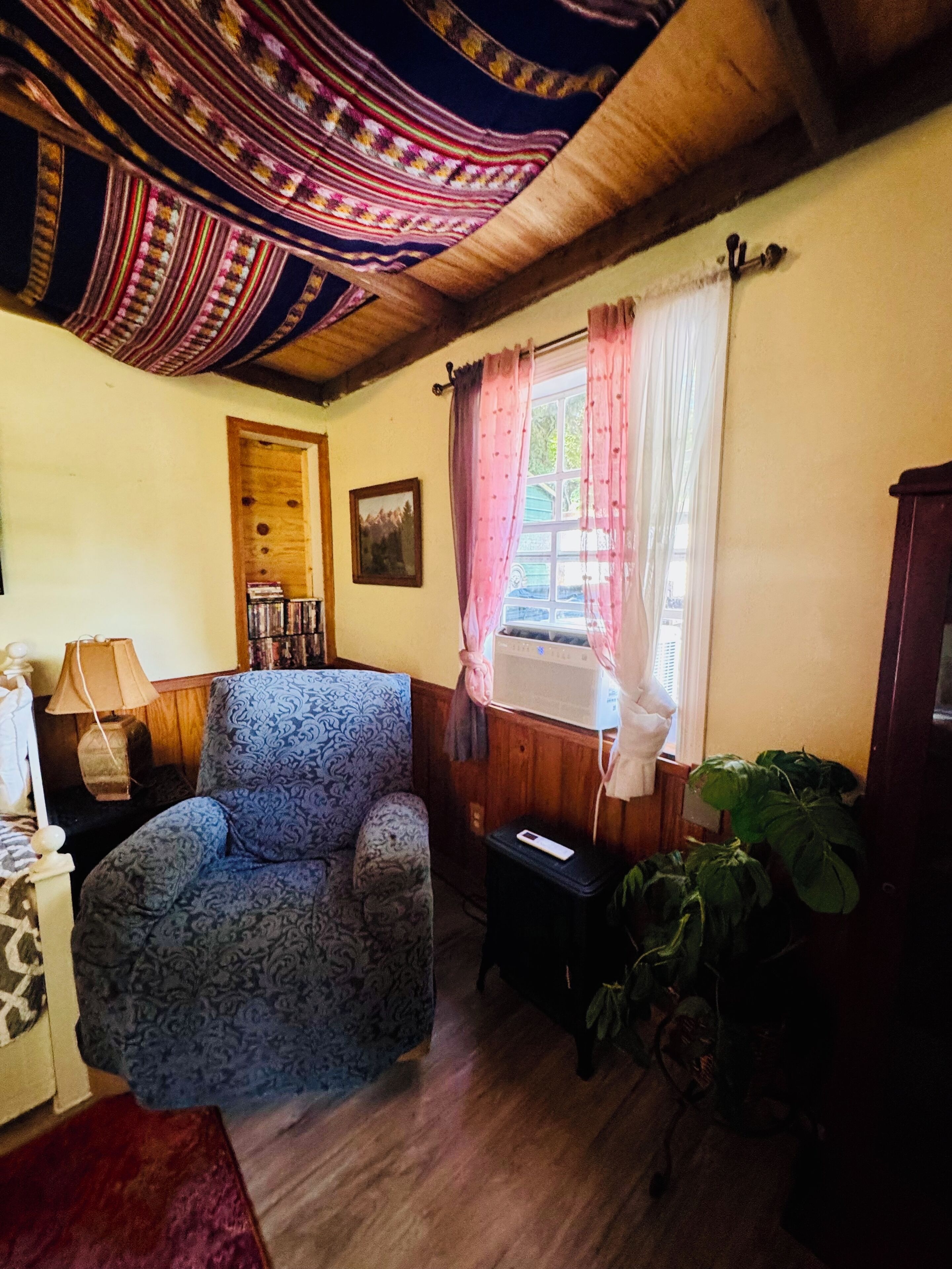 A cozy living room with a patterned armchair, a wooden cabinet, and a window with curtains.