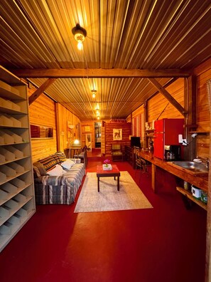 A cozy cabin interior with a wooden ceiling, a sofa, a dining table, and a kitchen area. - Ocala National forest  Fl-Pet friendly-Juanita’s Cabin  (Fort McCoy)
