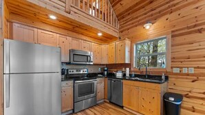 Une cuisine moderne dotée de meubles en bois, d’appareils électroménagers en acier inoxydable et d’une grande fenêtre qui laisse entrer la lumière naturelle.