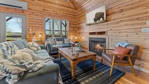 L’intérieur d’un chalet confortable, avec une cheminée, des murs en bois, un canapé, une table basse et une grande fenêtre.