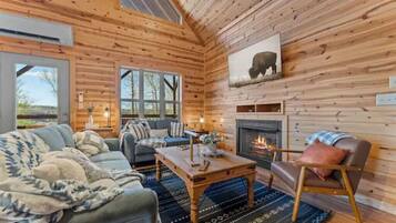 Ein gemütliches Blockhaus-Interieur mit Kamin, Holzwänden, einer Couch, einem Couchtisch und einem großen Fenster.