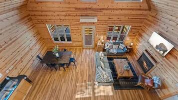 Una cabaña acogedora con interior de madera, una zona de comedor, un conjunto de sofás y una chimenea.