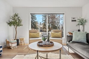 Un salon moderne avec une grande fenêtre, deux fauteuils, un canapé et une table basse.