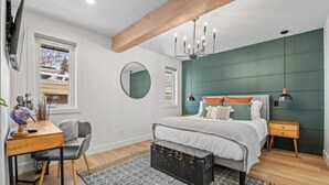A modern bedroom with a bed, a desk, a chair, a globe, and a large mirror. - The Duke | Spacious | Upscale | Close to DT (Calgary)