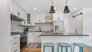 A modern kitchen with white cabinetry, stainless steel appliances, a central island with bar stools, and pendant lighting. - The Duke | Spacious | Upscale | Close to DT (Calgary)