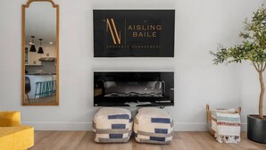 A modern living room with a large mirror, a framed logo, a fireplace, and a potted tree. - The Duke | Spacious | Upscale | Close to DT (Calgary)