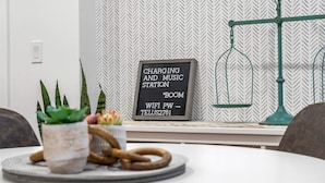 Une pièce moderne avec un mur orné d’un motif en chevrons, un panneau indiquant la présence d’une borne de recharge, une plante en pot et une lampe verte.