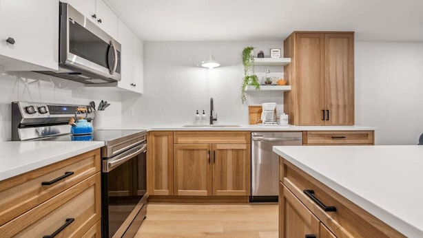 Une cuisine moderne avec des meubles en bois, des appareils en acier inoxydable et un plan de travail blanc.