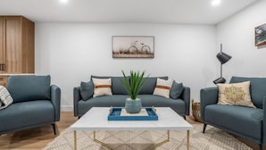 Un salon moderne avec deux canapés gris, une table basse blanche agrémentée de plateaux bleus, une plante en pot et une œuvre d’art représentant des bicyclettes, accrochée au mur.