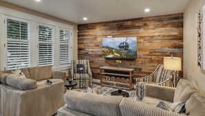 A living room with a wooden wall, a television, and a sofa. - Downtown Home + Mtn Views + Hot Tub + Ski Shuttle - Lansdowne Chateau (Breckenridge)