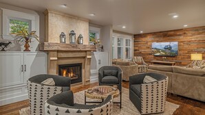 A living room with a fireplace, comfortable seating, a television, and a wooden accent wall. - Downtown Home + Mtn Views + Hot Tub + Ski Shuttle - Lansdowne Chateau (Breckenridge)
