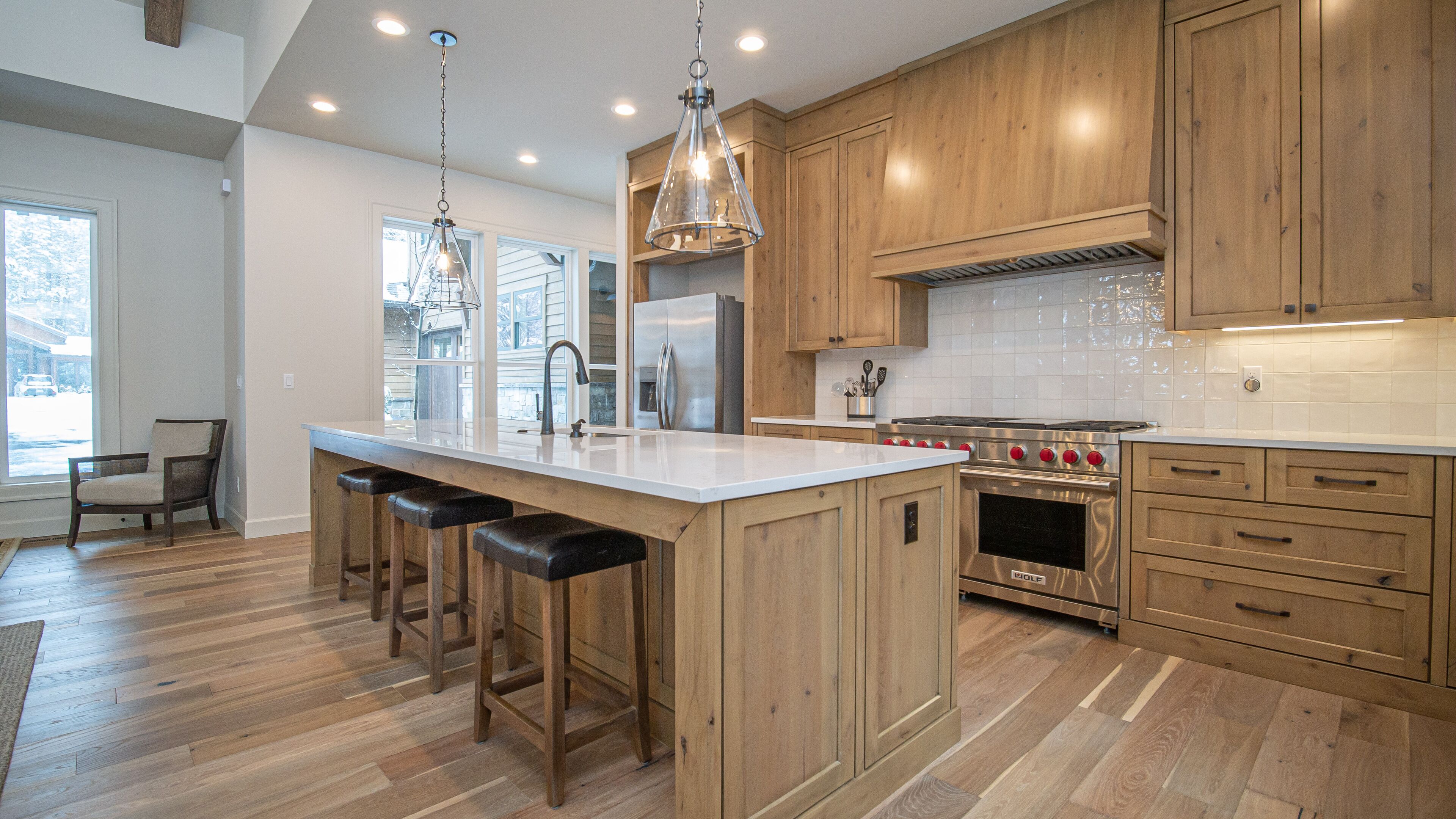 Une cuisine moderne avec des meubles en bois, un grand îlot central doté de tabourets, des appareils en acier inoxydable et un éclairage suspendu.