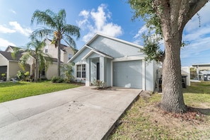 A residential house with a garage, a driveway, and a large tree in the front yard.
