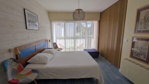 A bedroom with a bed, a chair, a hanging light fixture, and a window with curtains. - 42m² overlooking the pine forest and near the sea (Les Sables-d'Olonne)