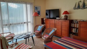 A living room with a television, wicker chairs, a sofa, and a bookshelf. - 42m² overlooking the pine forest and near the sea (Les Sables-d'Olonne)