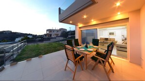 A modern outdoor dining area with a table and chairs, a glass balustrade, and a view of the surrounding landscape. - Villa Nelmar, Luxury Villas in Anavyssos (Athens)