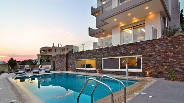 A modern pool area with a stone wall, lounge chairs, and a clear sky. - Villa Nelmar, Luxury Villas in Anavyssos (Athens)