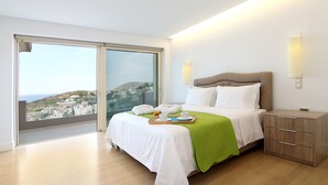 A bedroom with a large sliding glass door, a bed with white bedding and a green throw, a bedside table, and a nightstand. - Villa Nelmar, Luxury Villas in Anavyssos (Athens)