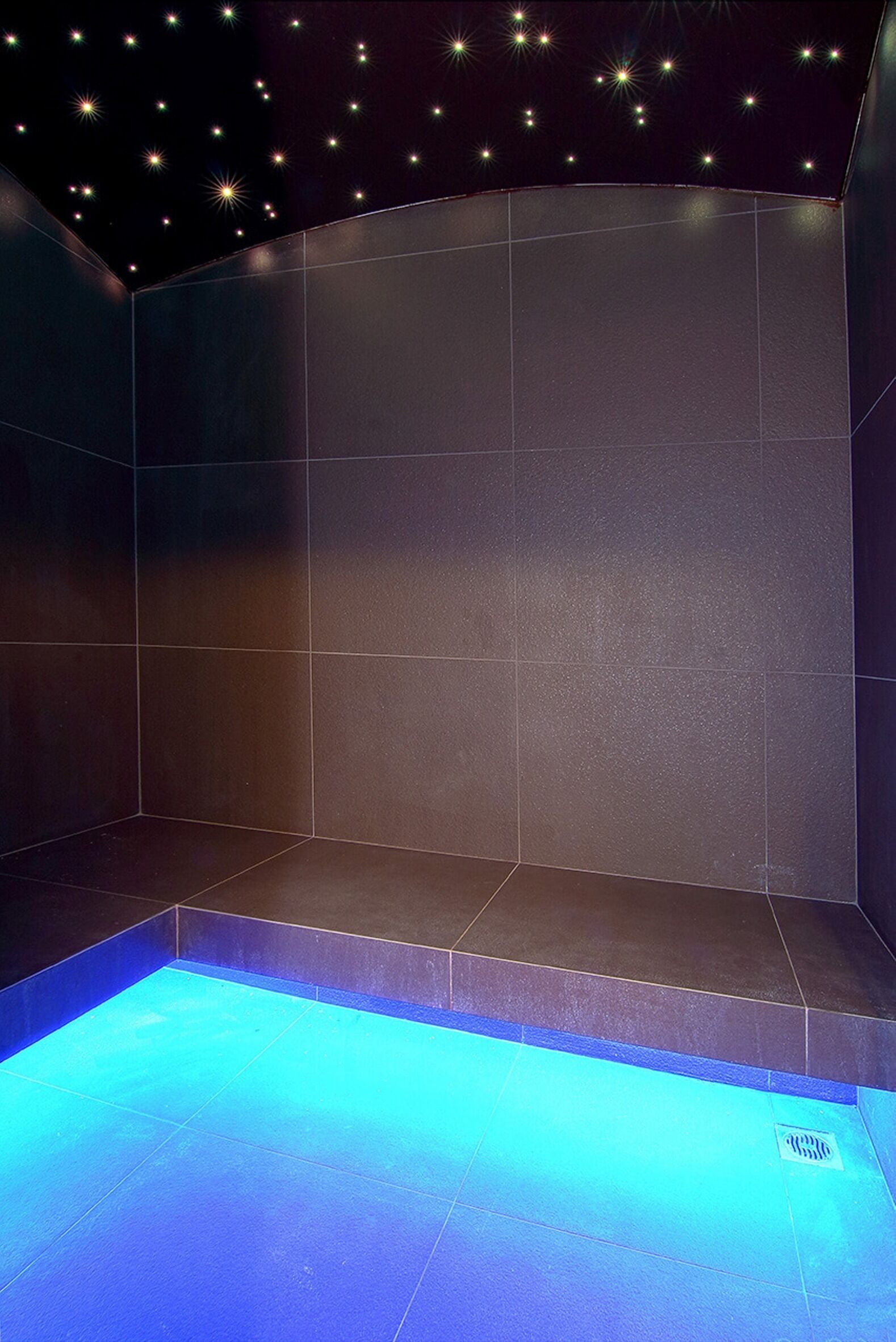 Ein modernes Badezimmer mit einem blau beleuchteten Pool, gefliesten Wänden und einer Sternenhimmel-Decke.
