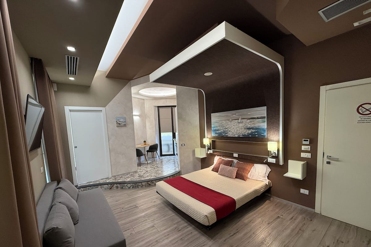Een moderne hotelkamer met een bed, een bank, een schilderij en uitzicht op zee.