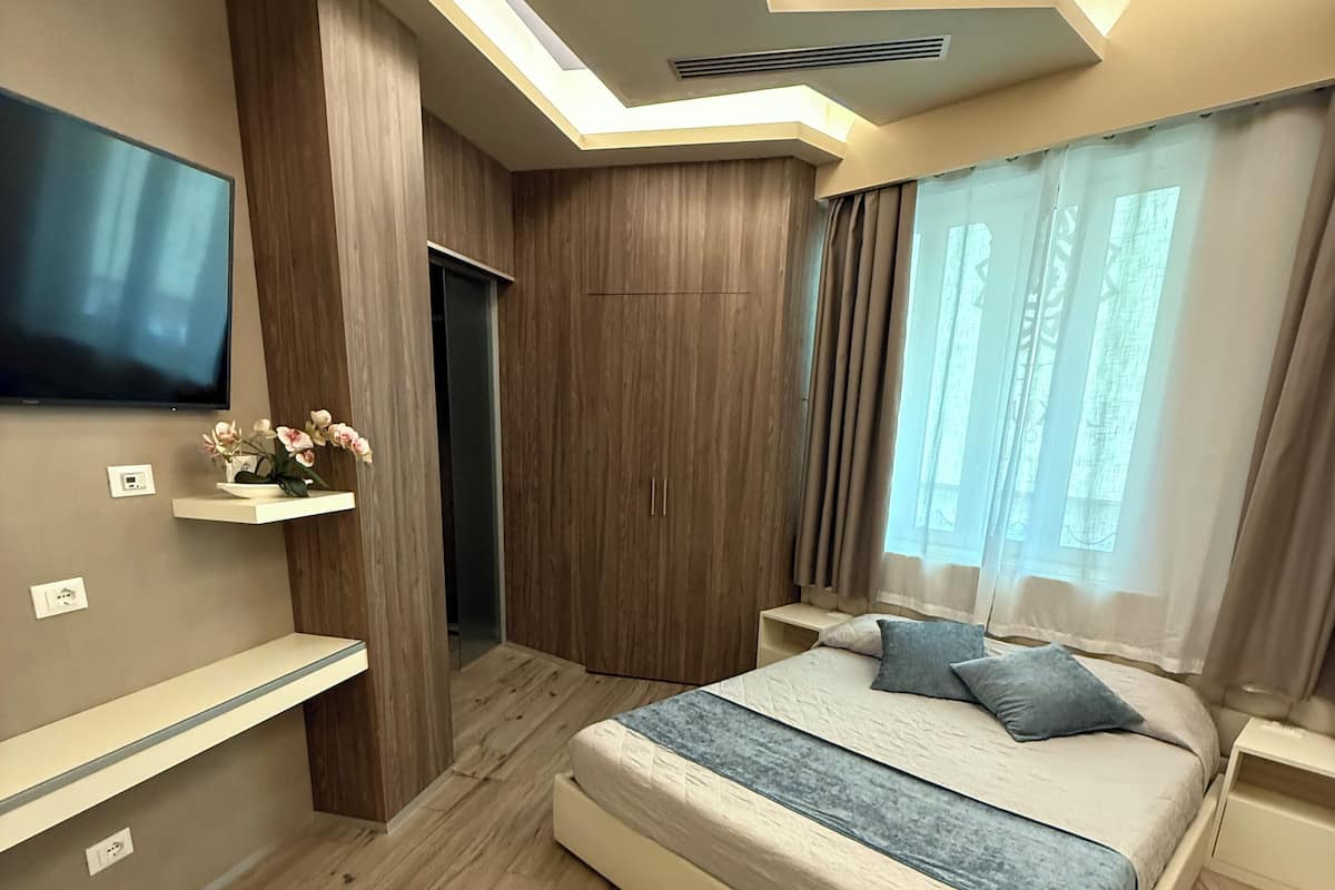 Een moderne slaapkamer met een groot bed, inbouwkasten, een flatscreen televisie en een houten vloer.