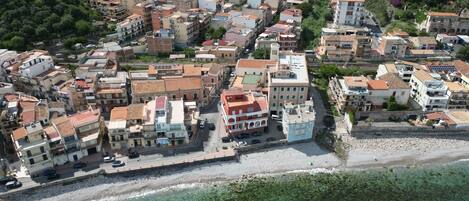 An aerial view of a coastal town with buildings along the waterfront, a beach, and clear turquoise waters.