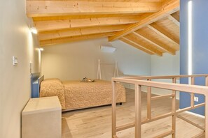 A small, cozy room with a sloped ceiling, a bed, a bedside table, and a window.