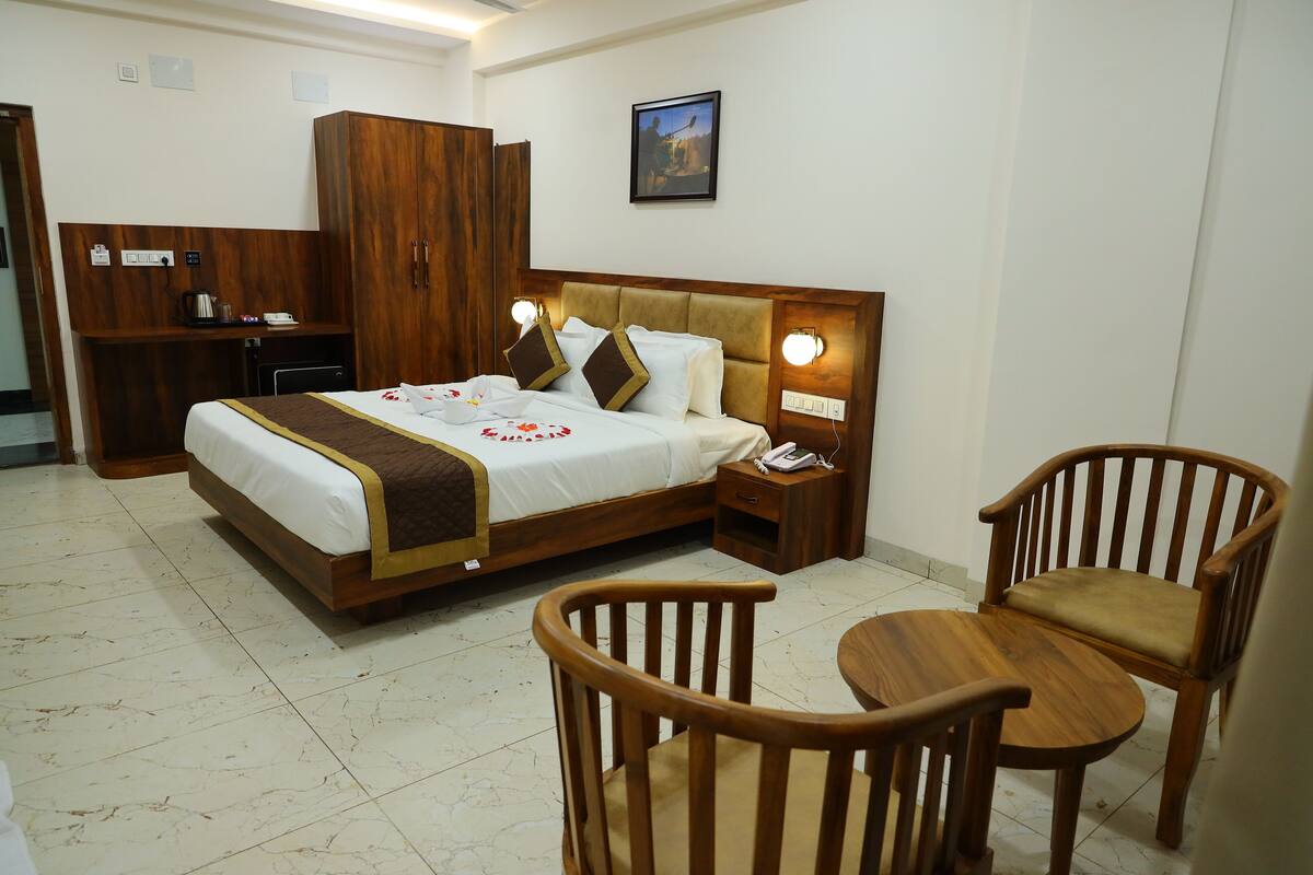 A hotel room with a bed, wooden wardrobe, bedside table, lamp, and two wooden chairs.