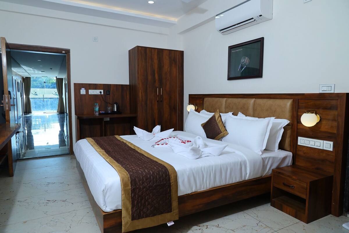 A hotel room with a large bed, wooden headboard, bedside tables, a wardrobe, and an air conditioning unit.