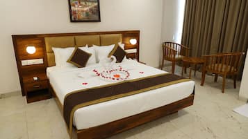 Una cama bien tendida con cabecera marrón, ropa de cama blanca y almohadas decorativas con forma de cisne. Hay dos mesitas de noche con lámparas, una silla y una pequeña mesa.