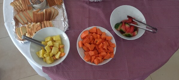 A table with a checkered tablecloth, three white plates with food items, and a foil tray with bread slices.