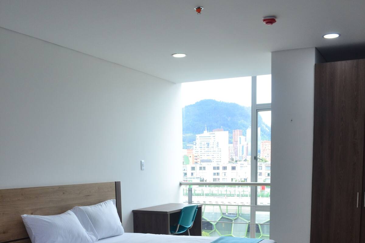 A hotel room with a large bed, a view of the city, and a wooden headboard.