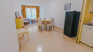 Una cocina compacta con refrigerador, mesa, sillas y un mueble pequeño.